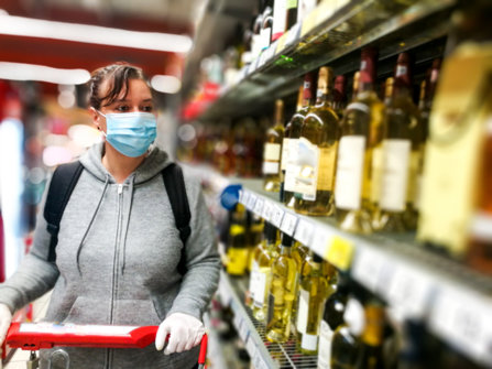 An alcoholic is shopping at store in a mask at the liquor section